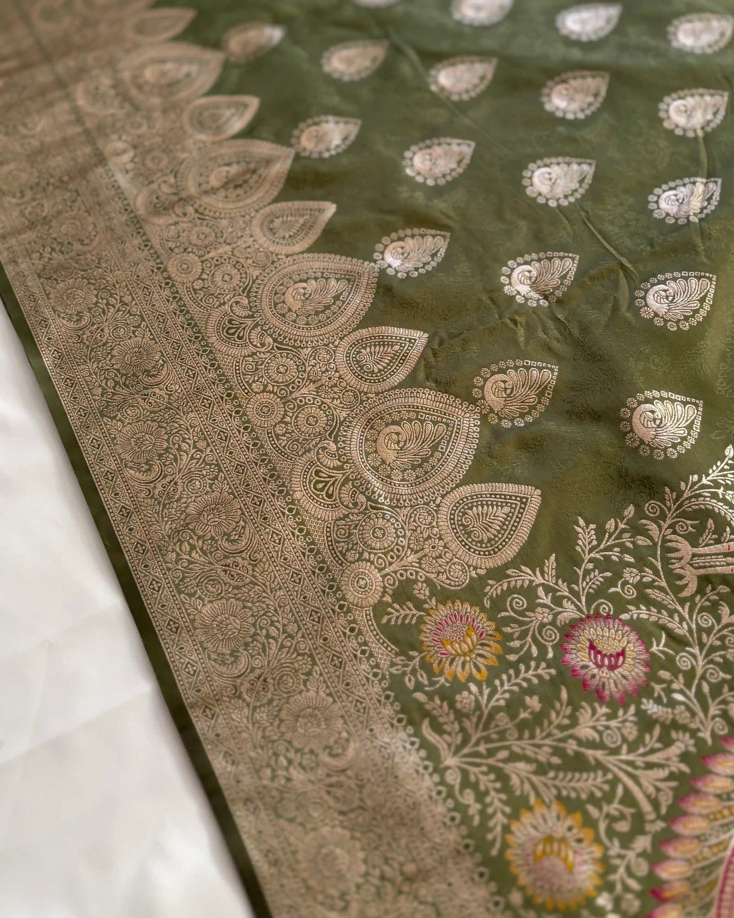 Close-up of a green fabric with intricate gold and multicolor embroidery on a white background