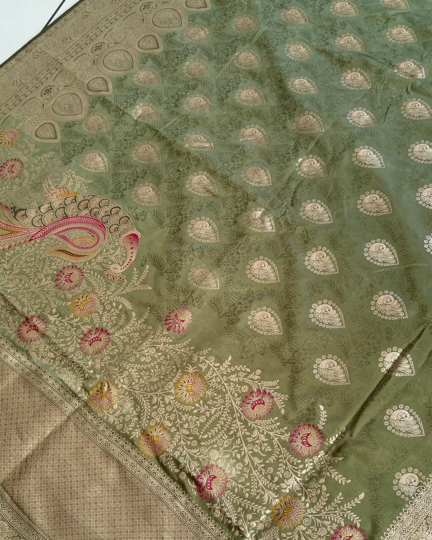 Green fabric with intricate white embroidery and pink floral patterns
