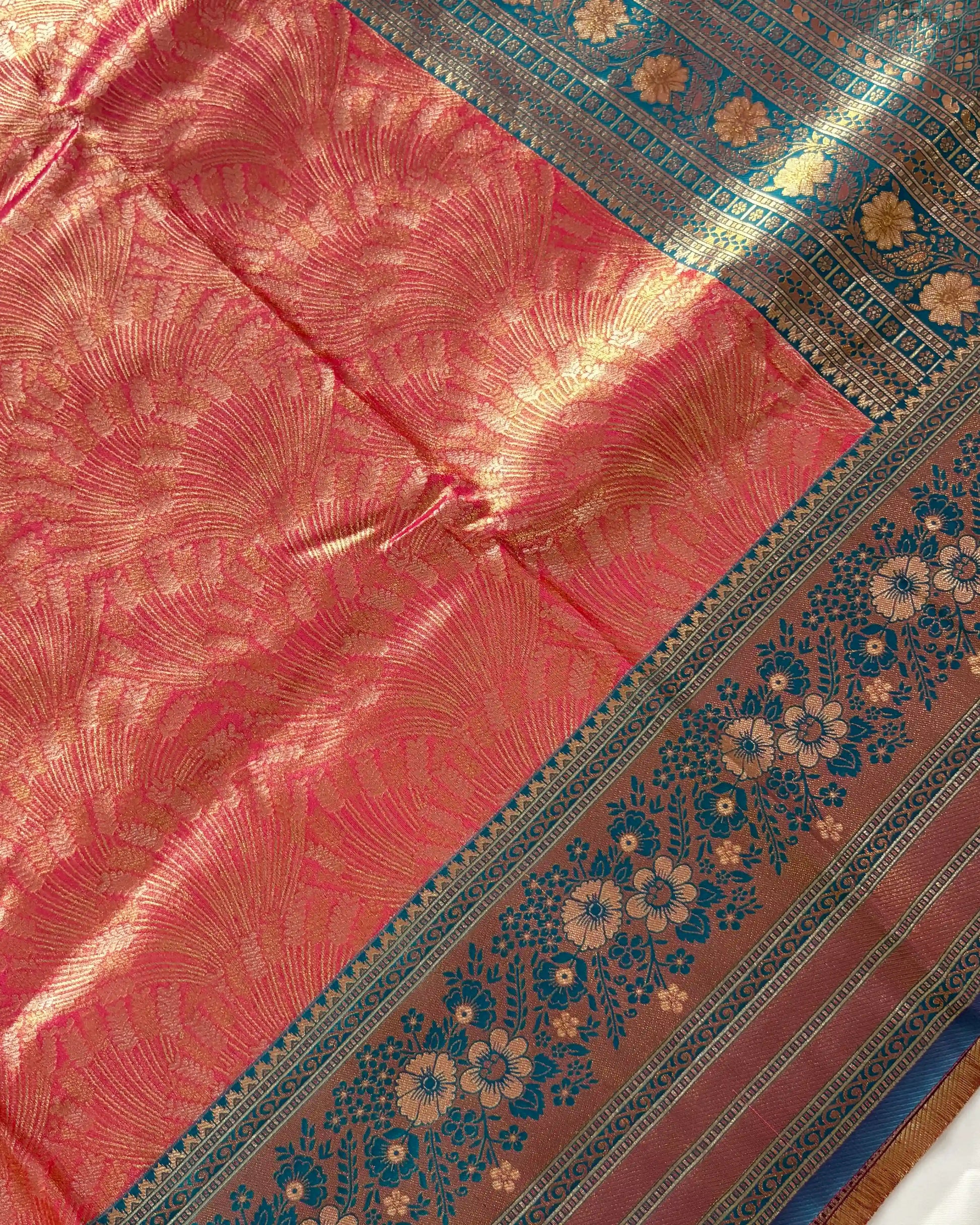 Close-up of a pink fabric with intricate patterns and a blue border featuring floral designs.