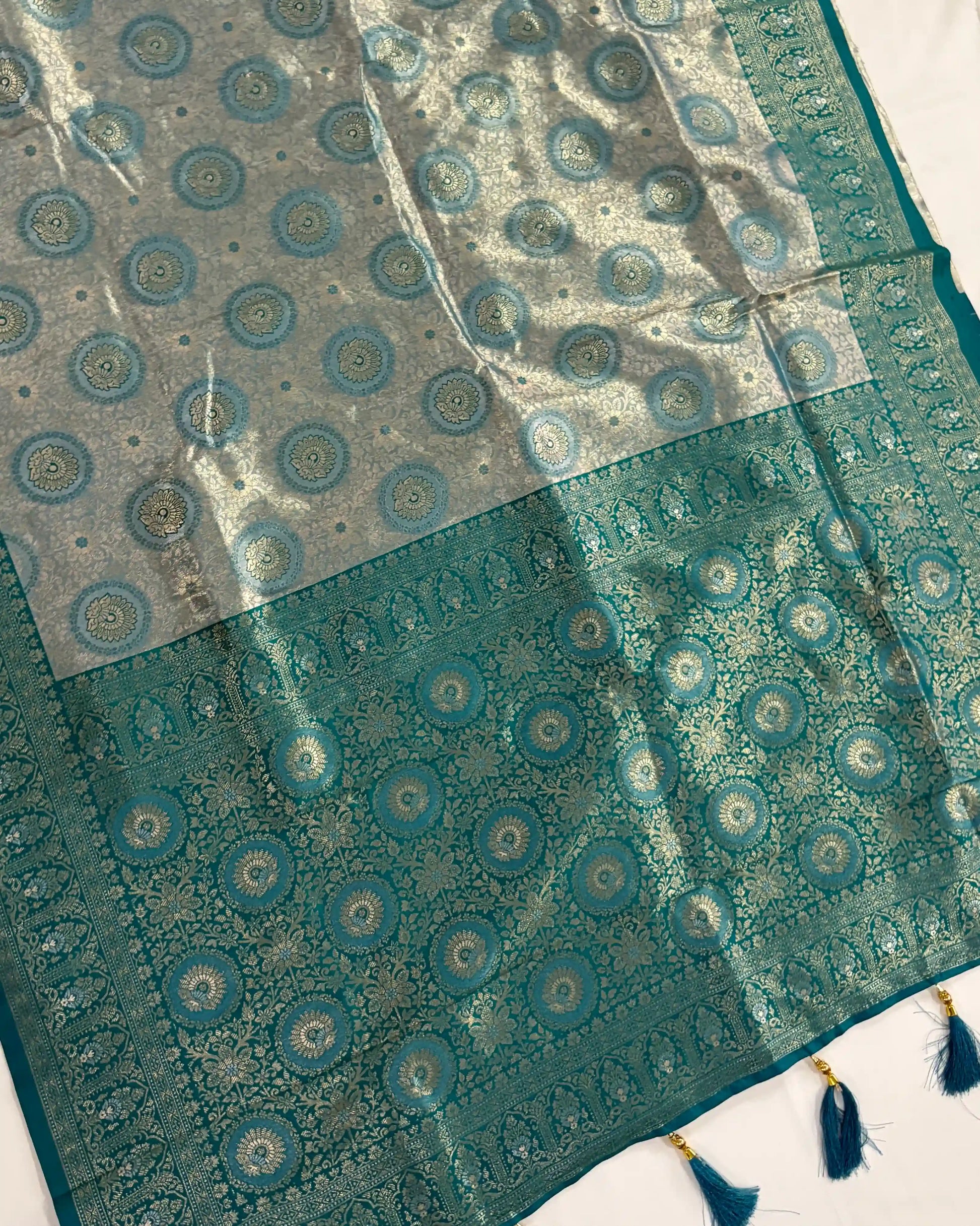Teal fabric with circular patterns and tassels on a white background